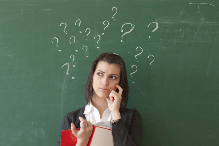 Image of student standing in front of a chalkboard with question marks written on the board